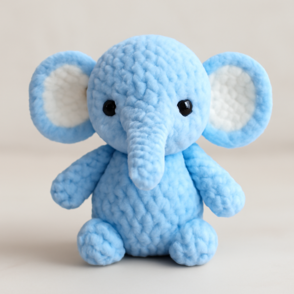 A light blue crocheted baby elephant toy with prominent trunk, long floppy ears, and safety eyes.