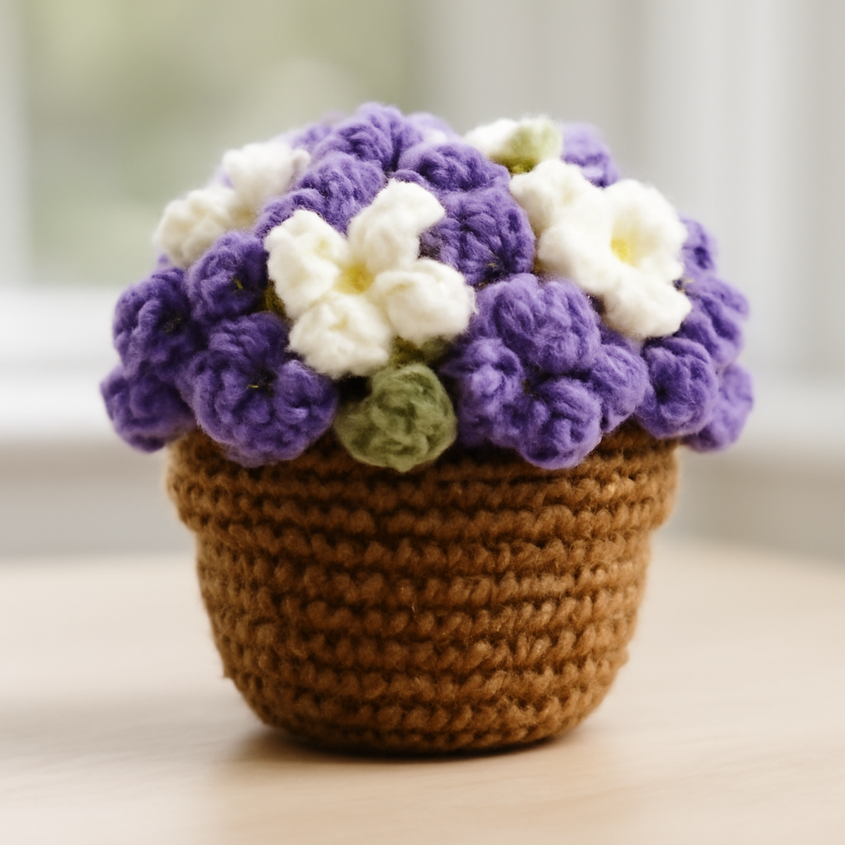 A charming crochet flower pot featuring purple, white, and green flowers, showcasing puff and slip stitches, with green leaves and a textured design.