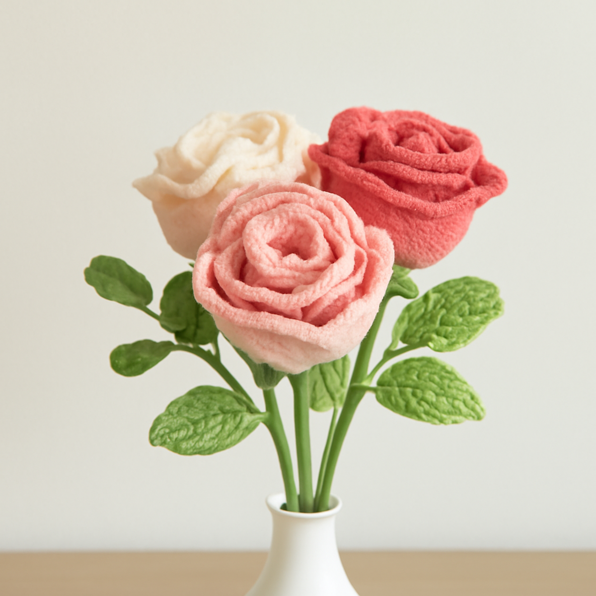 Crochet Wineglass Roses in pink, white, and coral colors arranged elegantly. Each rose has layered petals and green leaves, showcasing various crochet techniques.