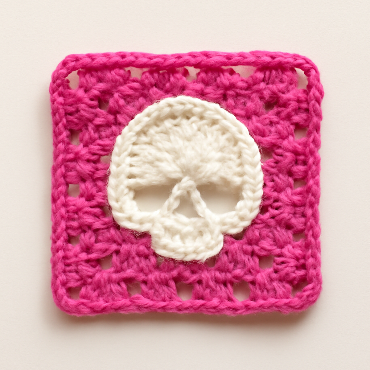 A Spooky Skull Crochet Square in pink and off-white, measuring approximately 6-8 inches, displaying a skull motif with a colorful border.